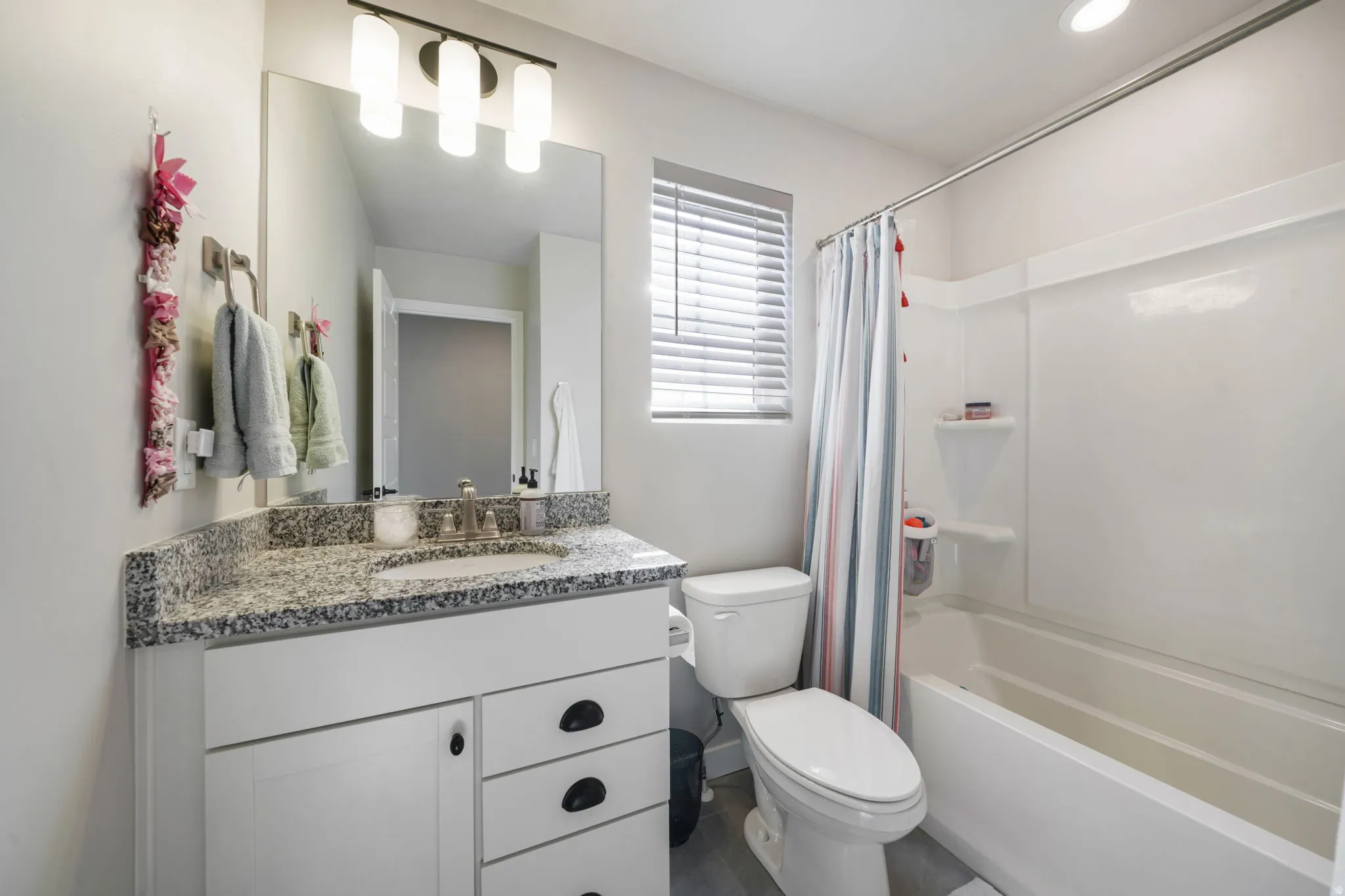 Vanity with granite-style countertop, undermount sink, and dark hardware