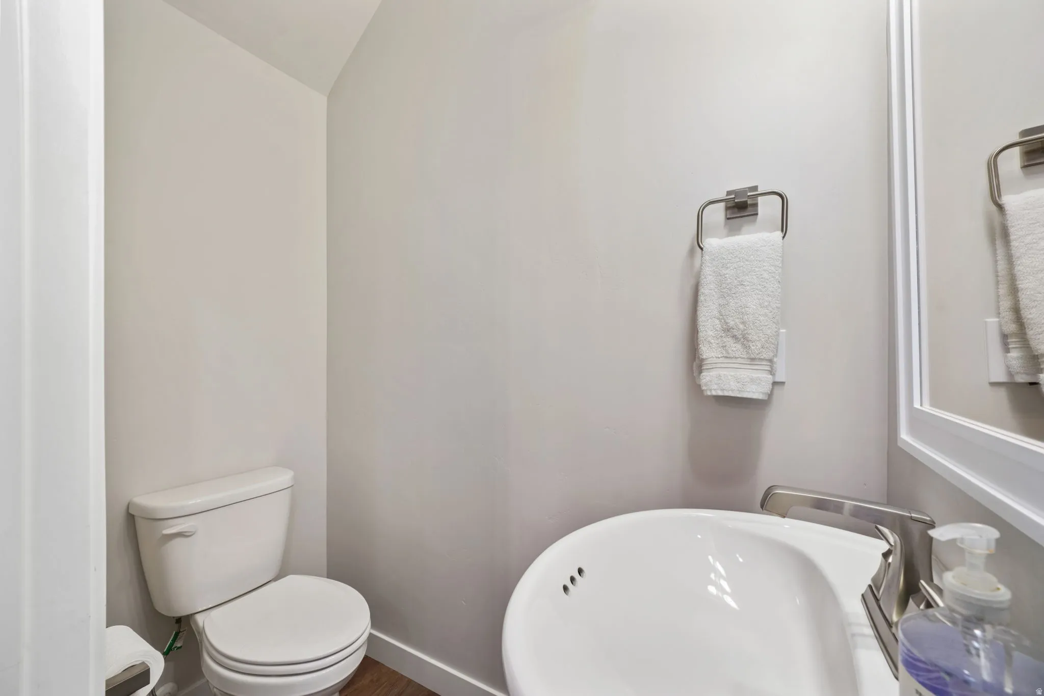 White toilet with a round bowl, a wall-mounted towel ring, and wood-finish flooring