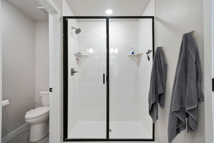 Walk-in shower with black-framed glass enclosure, white subway tile surround, and recessed lighting