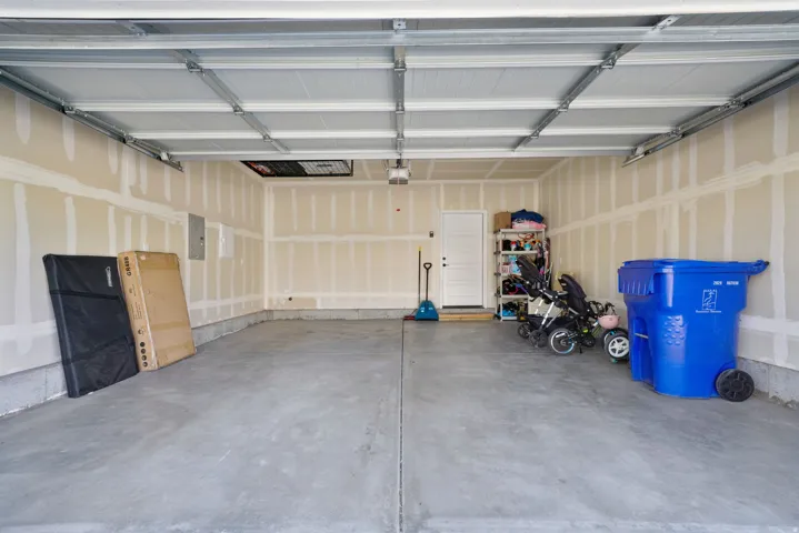 Spacious garage with exposed drywall, concrete flooring, and a white interior door