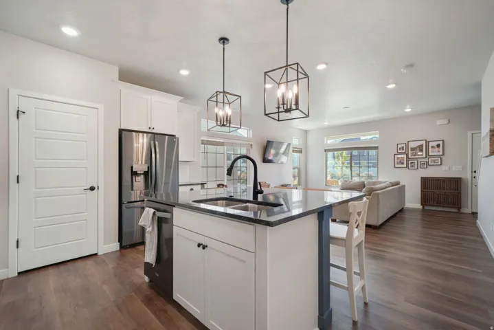 Kitchen island with integrated sink, stainless steel appliances, white cabinetry, wood-finish flooring, and recessed lighting