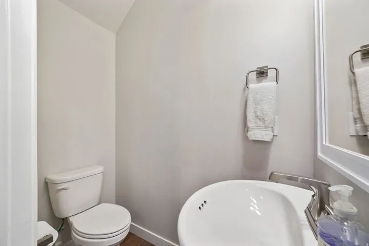 White toilet with a round bowl, a wall-mounted towel ring, and wood-finish flooring