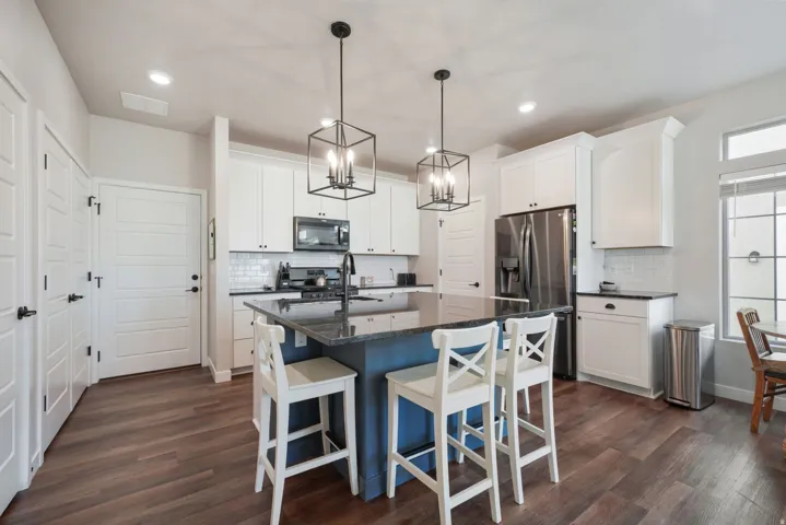 Kitchen featuring dark wood-finish flooring, white cabinetry, stainless steel appliances, dark countertops, and a central island with pendant lighting