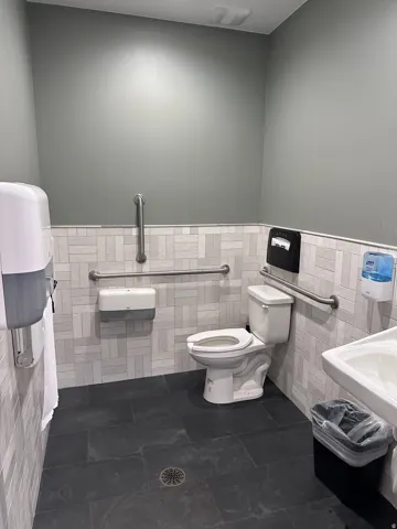 Floor-mounted toilet, dark tile flooring, light-toned tile wainscoting, and wall-mounted grab bars