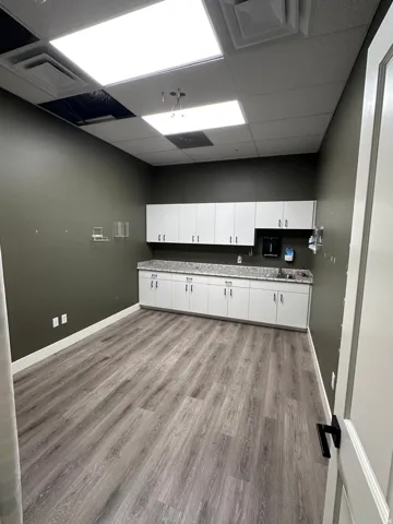Wood-finish flooring with white baseboards, ample white cabinetry, and light-colored countertops
