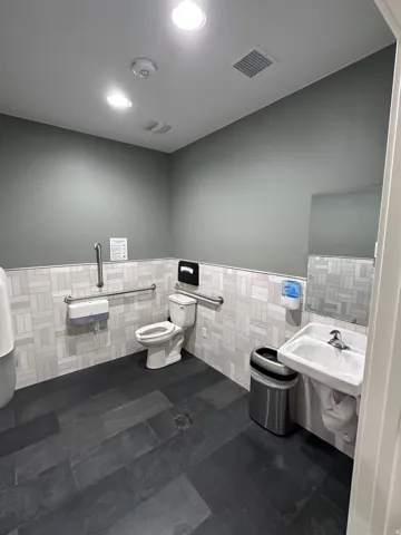 Dark slate-style tile flooring, white rectangular wall tile with a basketweave pattern, wall-mounted sink, toilet, and recessed ceiling lighting