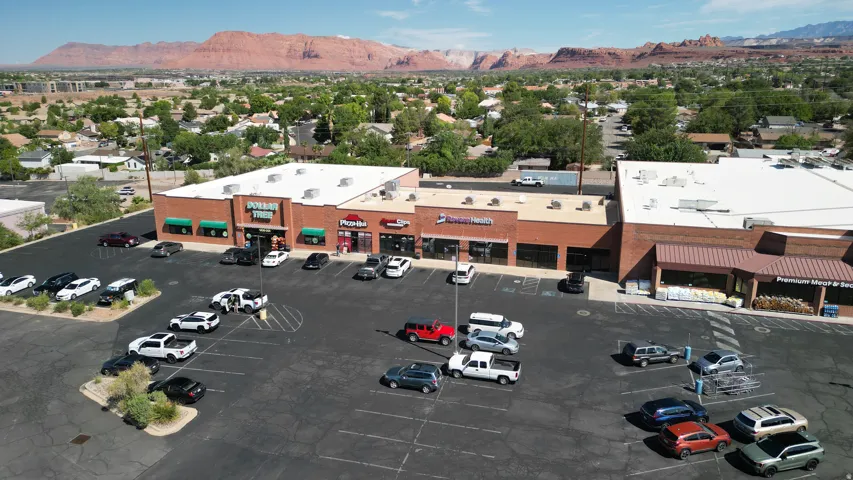 Commercial property with multiple storefronts, extensive paved parking, and visible mountain scenery