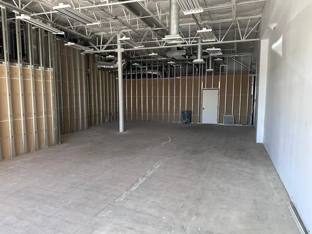 Spacious commercial interior featuring exposed ceiling trusses, visible ductwork, concrete flooring, and metal stud framing