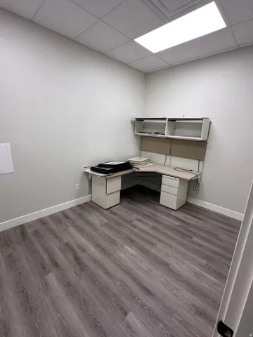Wood-finish flooring, drop ceiling with integrated lighting, and a built-in L-shaped desk with upper shelving