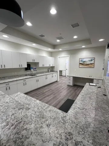 Modern kitchen featuring white cabinetry with brushed nickel hardware, speckled quartz countertops, recessed ceiling lighting, stainless steel appliances, and wood-finish flooring throughout the open-concept space