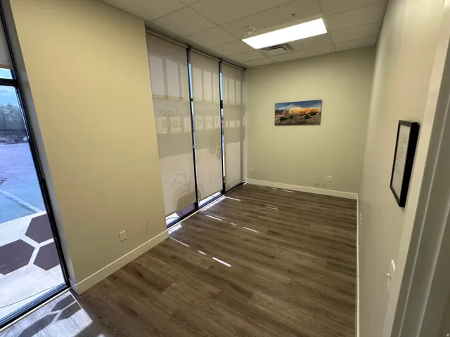 Wood-finish flooring with white baseboards, full-height windows with roller shades, and a drop ceiling with recessed lighting