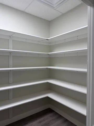 White wall-to-wall shelving with multiple tiers, wood-finish flooring, and white painted walls