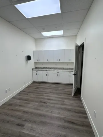 Wood-finish flooring, white cabinetry, integrated overhead lighting, and stone-finish countertops