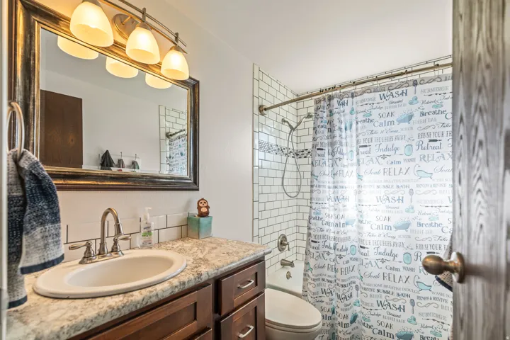 Vanity with wood-finish cabinetry, oval sink, and a framed mirror with overhead lighting