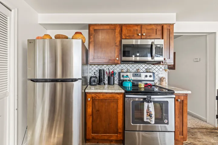 Stainless steel appliances, wood cabinetry, granite countertops, and a decorative tile backsplash
