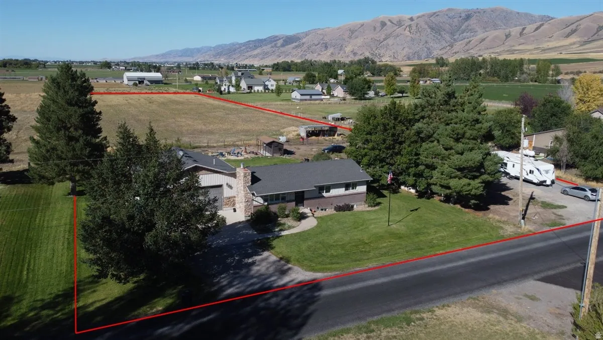 Expansive property featuring a single-story residence with a stone chimney, a detached garage, and a large paved driveway