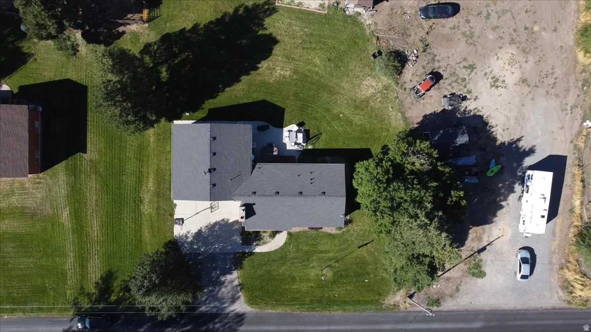 Property featuring a dark gray shingle roof, expansive green lawn, mature trees, and a paved driveway