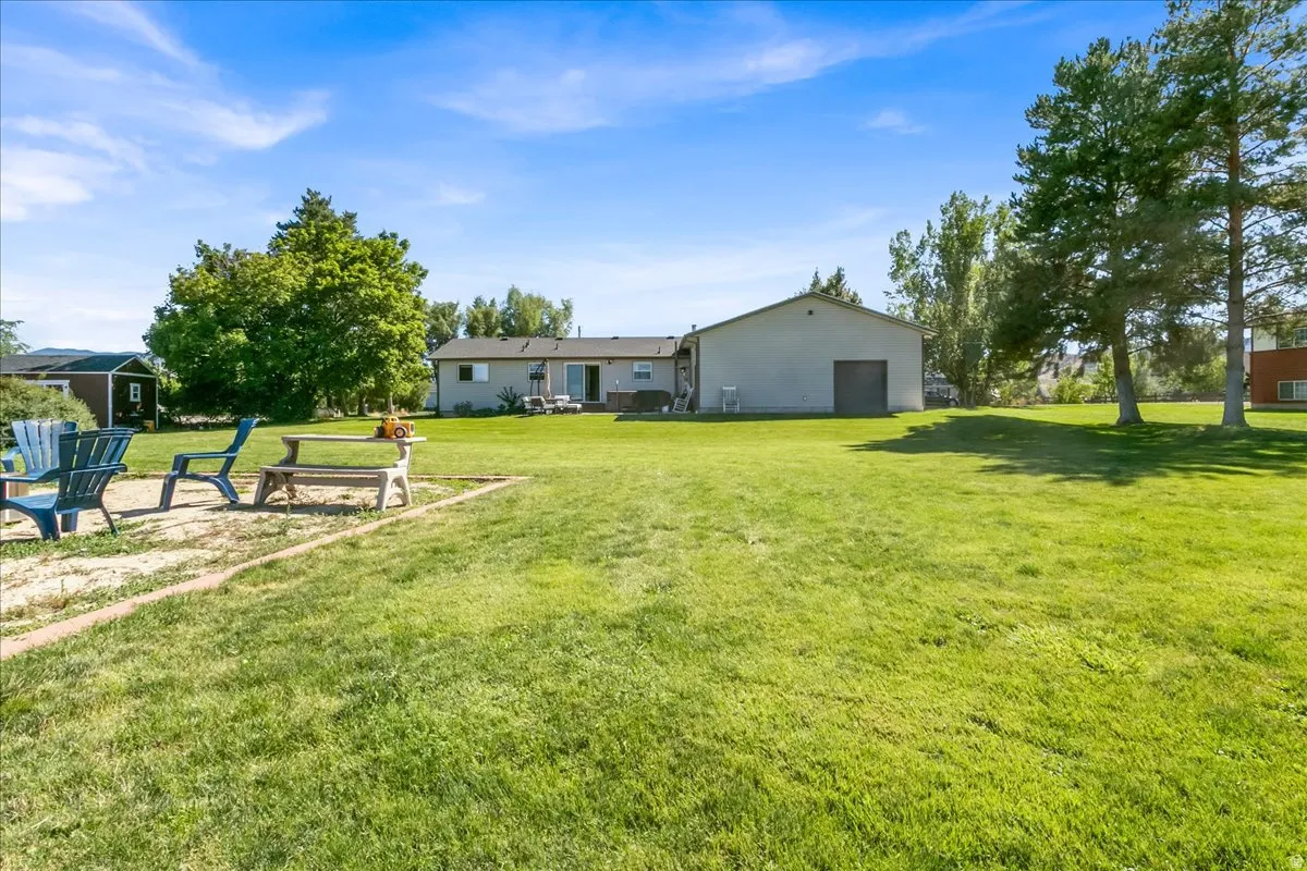 Expansive green lawn with mature trees and a detached structure featuring a roll-up door