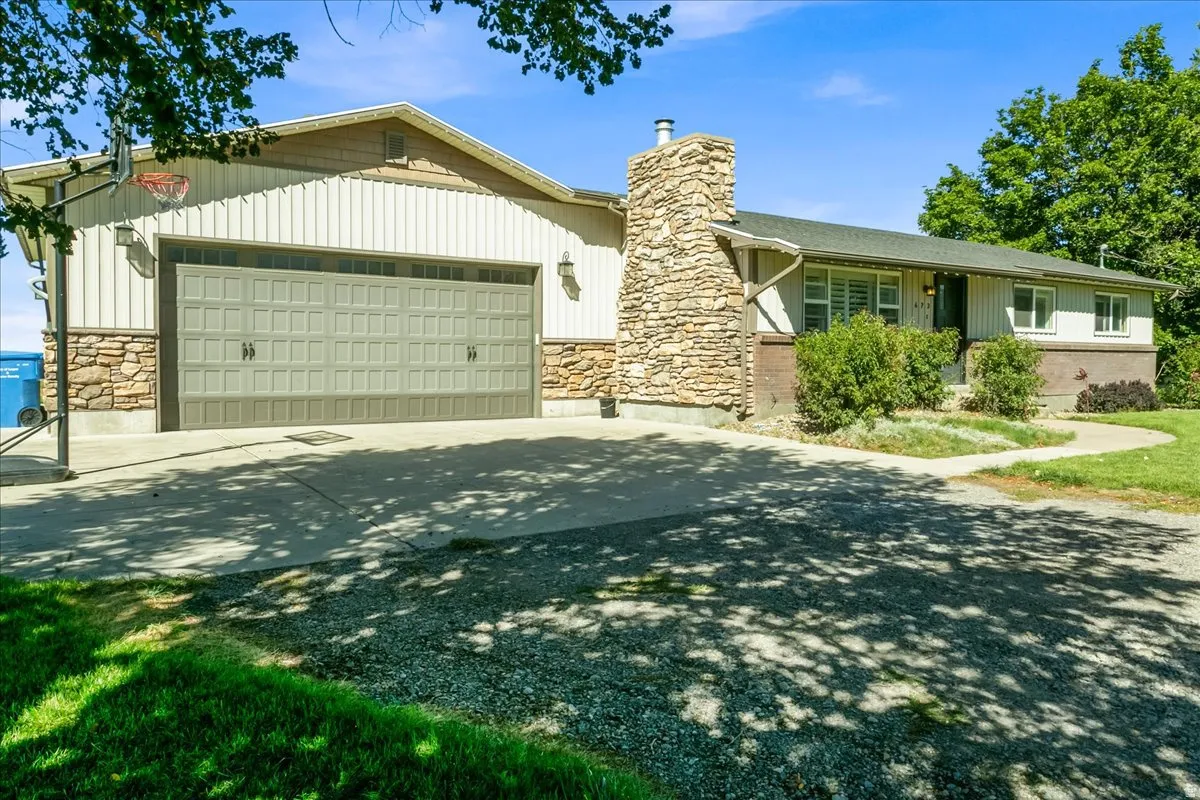 Exterior featuring a large attached garage, stone veneer siding, vertical panel siding, a stone chimney, and a concrete driveway