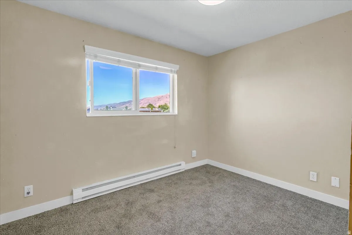 Light-colored walls, grey textured carpeting, and a white window frame with a mountain backdrop