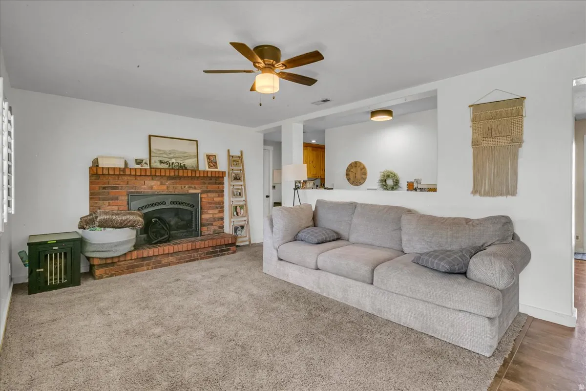 Brick fireplace with hearth, ceiling fan with integrated lighting, recessed wall opening, and carpeted flooring