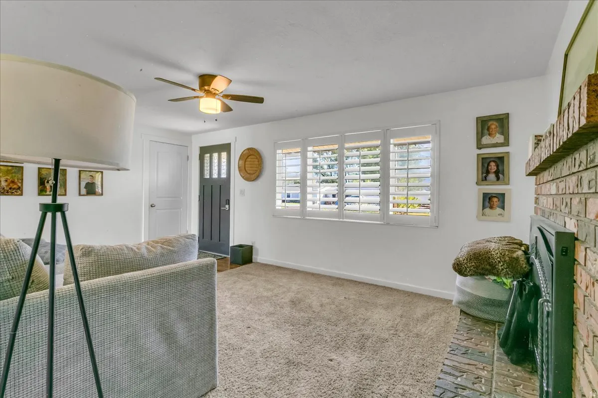 Built-in brick fireplace with a black firebox, multiple windows with white plantation shutters, and a ceiling fan with integrated lighting