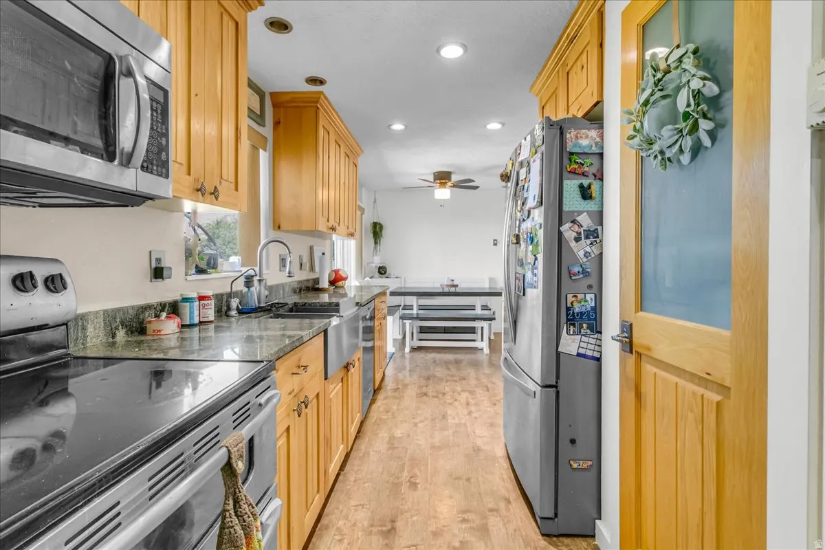 Kitchen featuring wood-finish cabinetry, stainless steel appliances, a farmhouse sink, stone countertops, and wood-finish flooring