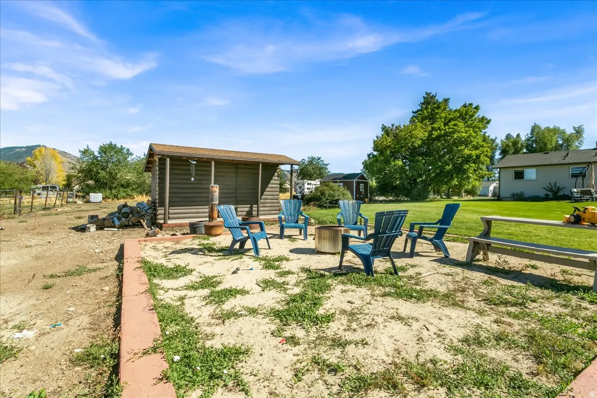 Expansive outdoor area featuring a fire pit, log-style shed with an overhang, a large grassy area, and mature trees