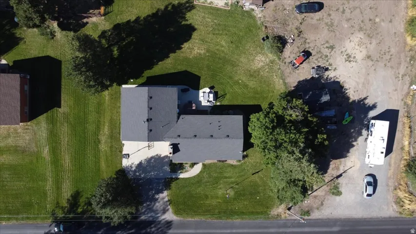 Property featuring a dark gray shingle roof, expansive green lawn, mature trees, and a paved driveway
