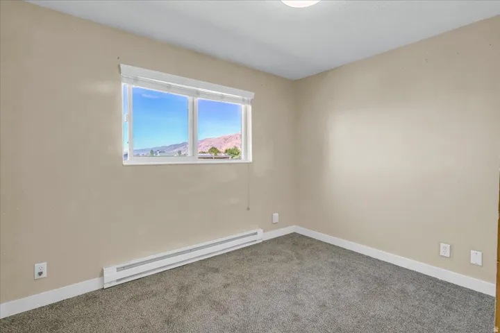 Light-colored walls, grey textured carpeting, and a white window frame with a mountain backdrop