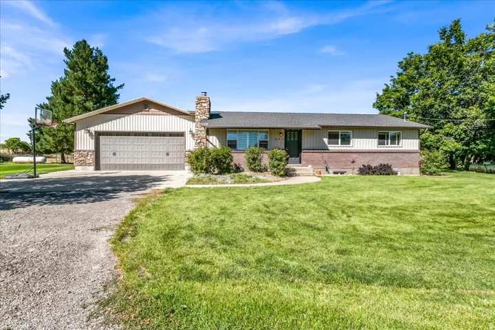 Single-story residence featuring a two-car garage, stone chimney, and a gravel driveway