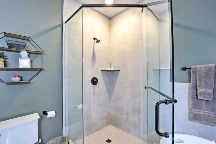Glass-enclosed shower with matte black fixtures, integrated shelving, and tile flooring