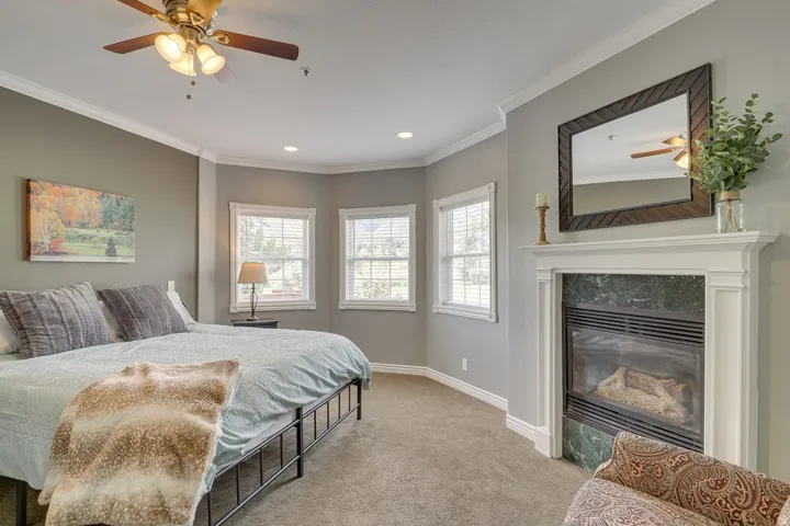 Fireplace with a stone surround and white mantel, multiple windows, recessed lighting, crown molding, and a ceiling fan with integrated lighting
