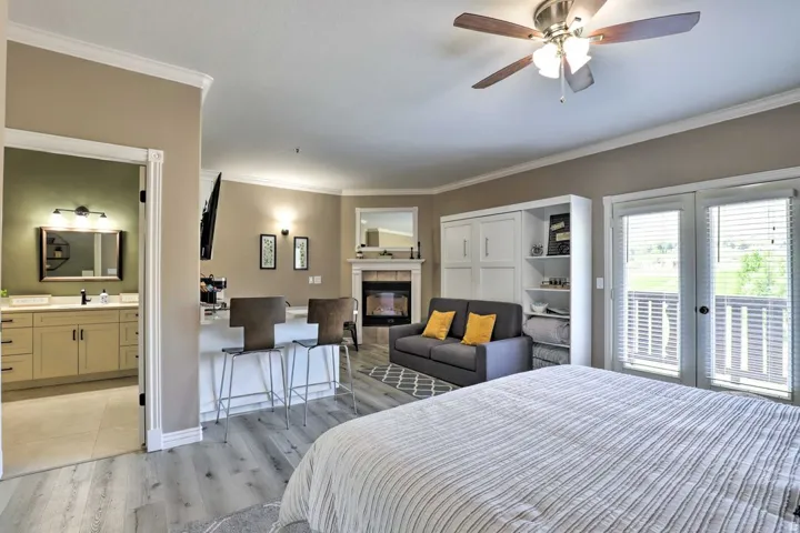 Light wood-finish flooring, built-in shelving, white double French doors with blinds, fireplace with mantel, and a ceiling fan