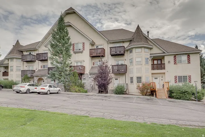 Multi-story building featuring light-colored stucco siding, multiple private balconies with wood railings, and decorative red and white shutters