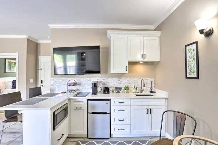 Compact kitchen area featuring white cabinetry, a built-in microwave, a stainless steel sink, a tiled backsplash, and a counter-height breakfast bar