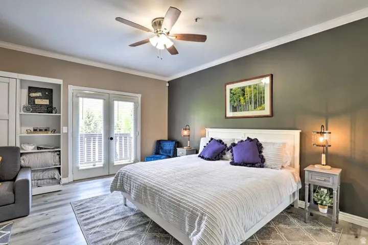 Wood-finish flooring, ceiling fan, white French doors, built-in shelving, and crown molding