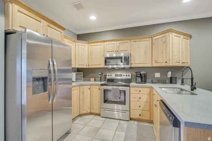 Kitchen featuring stainless steel appliances, light wood cabinetry, light-toned countertops, tile flooring, and a single-basin sink with a gooseneck faucet