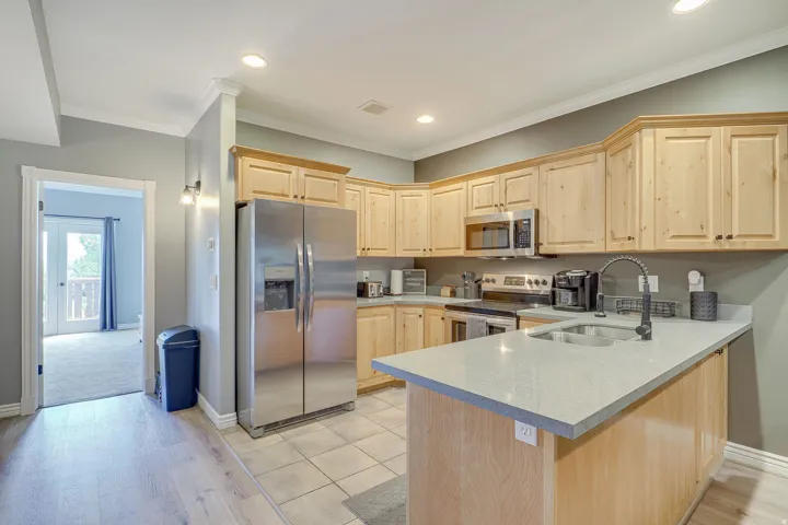 Kitchen featuring wood cabinetry, stainless steel appliances, light-toned countertops, and a built-in sink with a black faucet