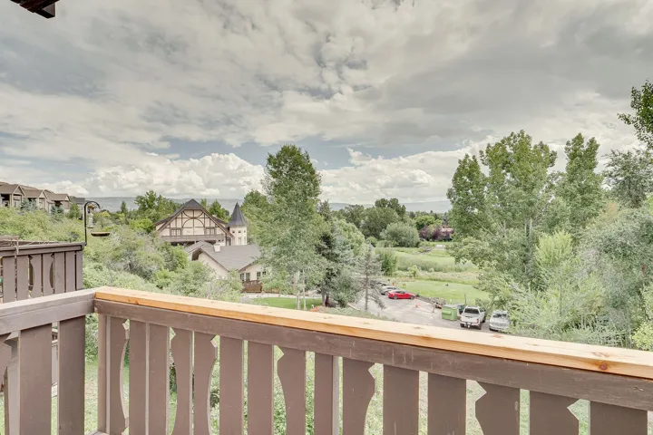 Balcony with wood railing overlooking a landscape with distant structures and mature trees