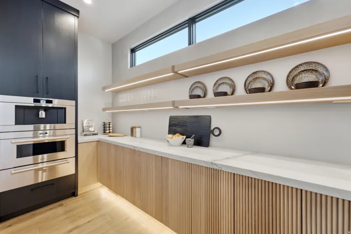 Built-in stainless steel appliances, light wood-finish open shelving with integrated lighting, wood-finish flooring, and a stone countertop