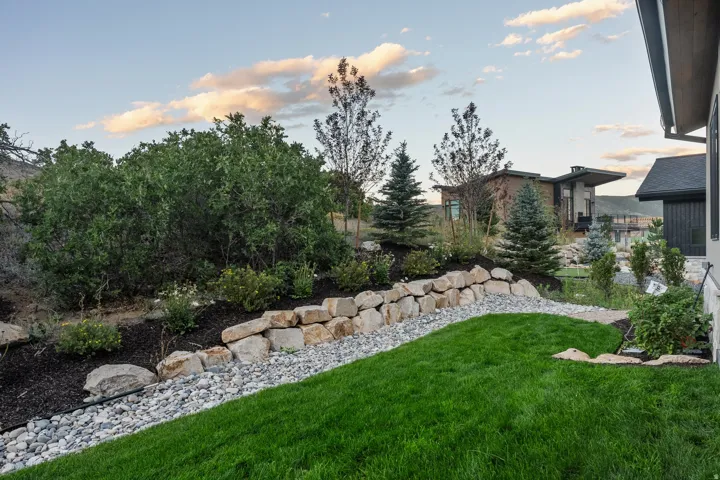 Landscaped property perimeter featuring a stone retaining wall and river rock drainage