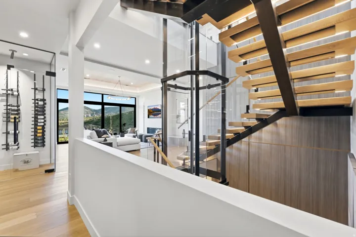 Modern open-riser staircase with wood treads and metal stringers, an integrated glass-enclosed elevator, built-in wine storage, and wide plank wood-finish flooring