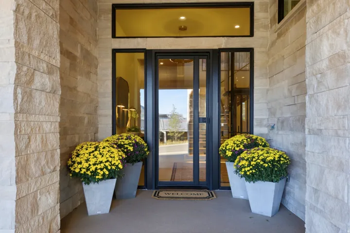 Stone veneer exterior with a glass-paneled entry door, transom window, and a concrete landing