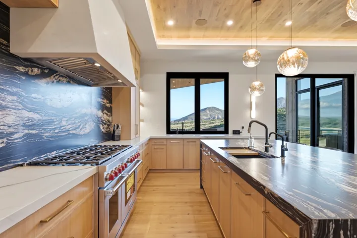 Gourmet kitchen featuring a large range with a custom hood, black marble backsplash, and light wood-finish flooring