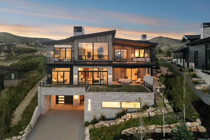 Multi-level modern residence featuring extensive glazing, wood-paneling, stone facade, multiple balconies, and integrated landscaping