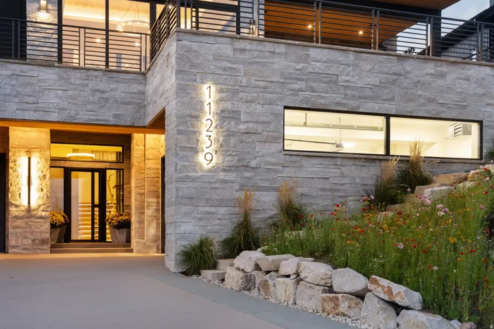 Stone-clad exterior with integrated house numbers, full-light entry door, and a second-level balcony with metal railings