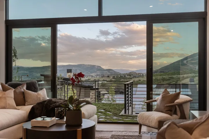 Expansive glass sliding doors open to an outdoor space with metal railings, offering a panoramic mountain backdrop