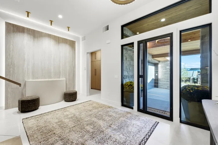 Entry foyer featuring a floor-to-ceiling accent wall with integrated lighting, expansive window panels with black frames, a wood-paneled ceiling element, and light-toned flooring