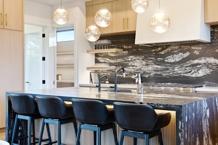 Kitchen featuring a large island, wood-finish cabinetry, a patterned natural stone backsplash, and pendant lighting